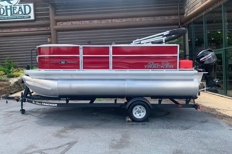 The Image of 2026 Sun Tracker Party Barge 16 DLX pontoon boat on trailer, red and silver design. - 0