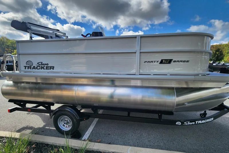 The Image of 2026 Sun Tracker Party Barge 16 DLX pontoon boat on trailer under cloudy sky. - 0