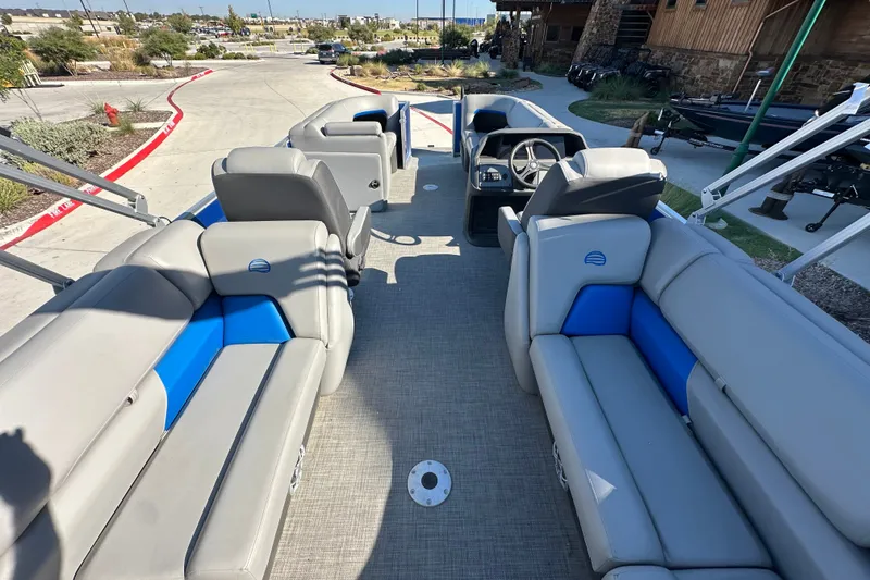 Slide: The Image of 2026 Sun Tracker Party Barge 22 DLX interior with gray and blue seating, docked outdoors. - 46