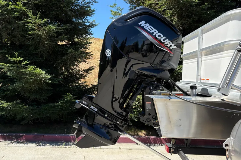 Slide: The Image of 2026 Sun Tracker Party Barge 18 DLX with Mercury outboard motor, parked near trees. - 30