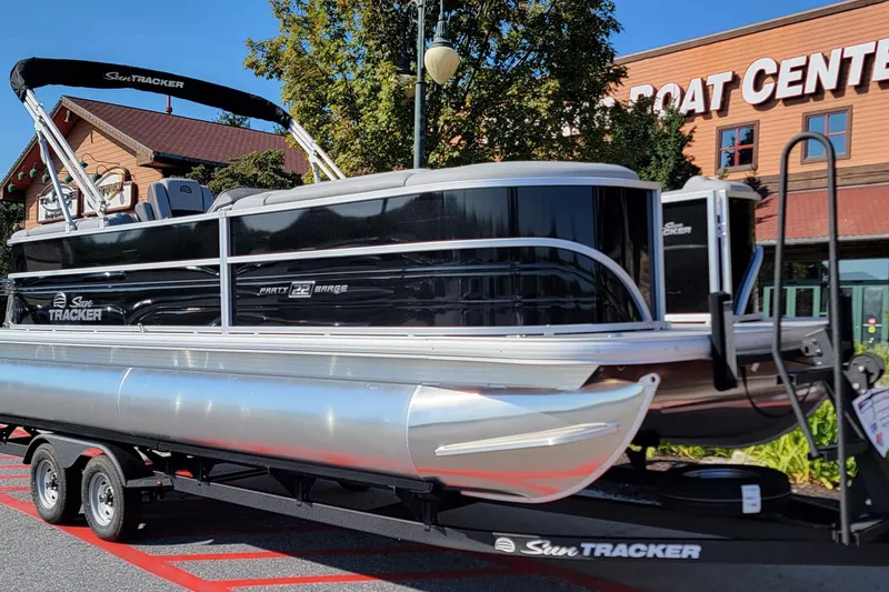The Image of 2026 Sun Tracker Party Barge 22 DLX pontoon boat at dealership, "We Take Trades" sign visible. - 0