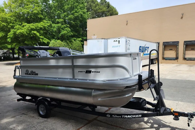 Slide: The Image of 2026 Sun Tracker Party Barge 16 DLX pontoon boat on trailer, parked outdoors. - 2
