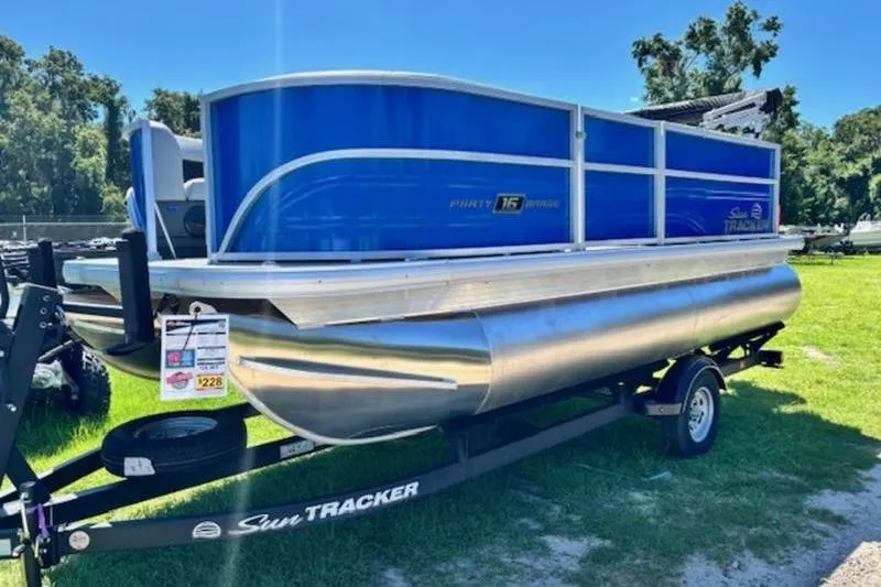 Slide: The Image of 2026 Sun Tracker Party Barge 16 DLX pontoon boat on trailer, parked on grass. - 2