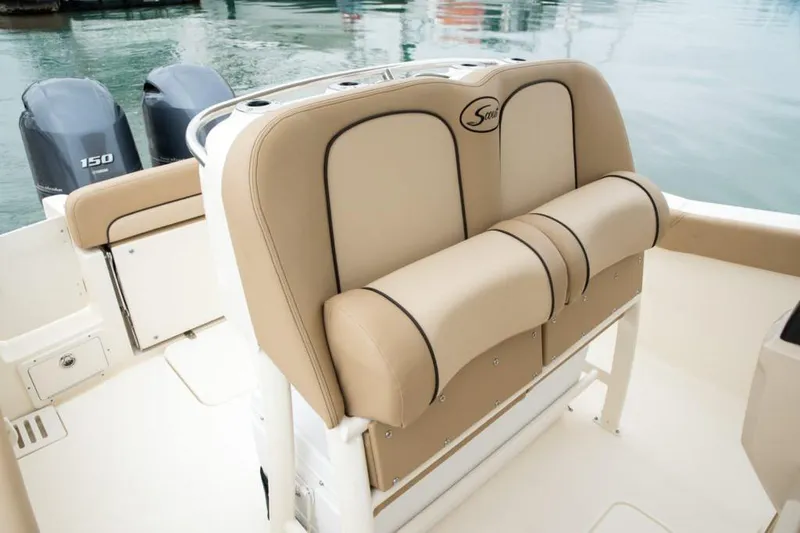 Slide: The Image of 2020 Scout 255 LXF boat with cushioned seating and windshield, parked near a road. - 8