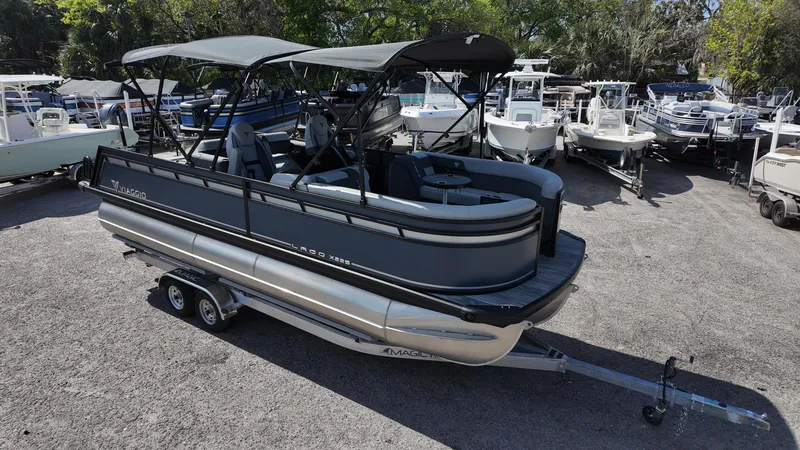Slide: The Image of 2025 Viaggio X22S pontoon boat on trailer, parked among other boats. - 2
