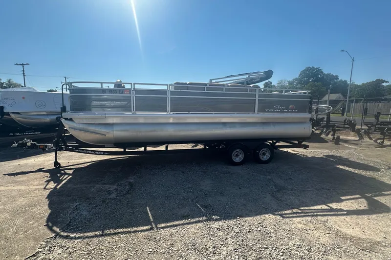 The Image of 2024 Sun Tracker Fishin' Barge 22 DLX pontoon boat on trailer, parked outdoors. - 0