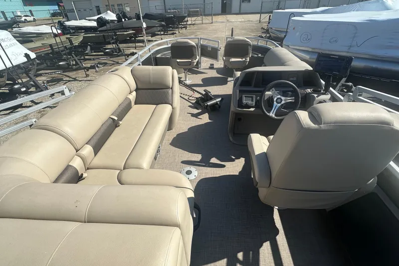 Slide: The Image of 2024 Sun Tracker Fishin' Barge 22 DLX interior with beige seating and steering console. - 18