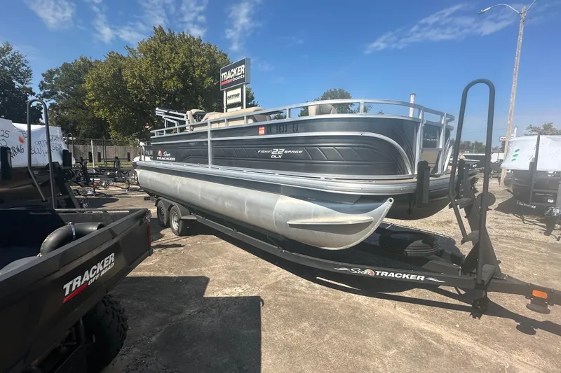 Slide: The Image of 2024 Sun Tracker Fishin' Barge 22 DLX pontoon boat on trailer, outdoor display. - 2