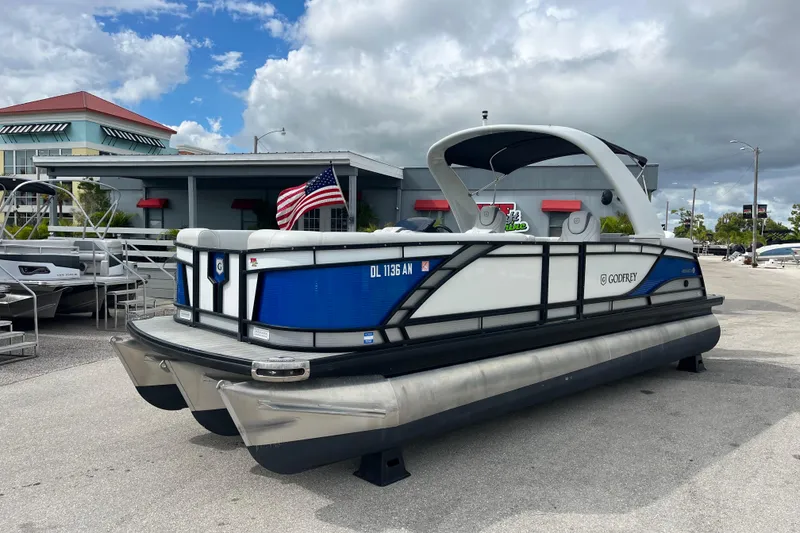 The Image of 2021 Godfrey Monaco 255 RL Tri Toon pontoon boat with American flag, parked outdoors. - 1