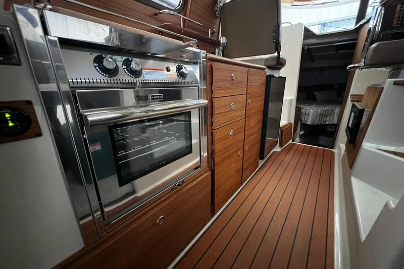 Slide: The Image of 2025 Ranger Tugs R-27 interior with modern kitchen, wood cabinetry, and stainless steel oven. - 17