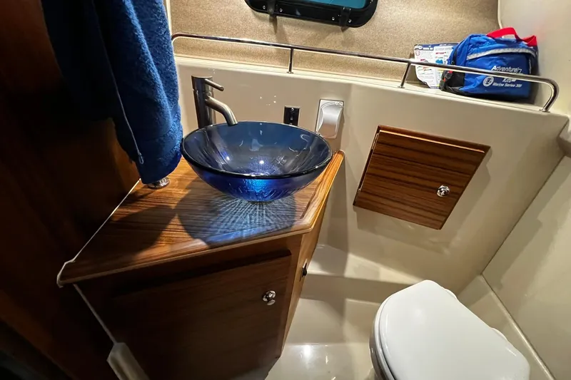 Slide: The Image of 2025 Ranger Tugs R-27 bathroom with blue glass sink and wooden cabinetry. - 24