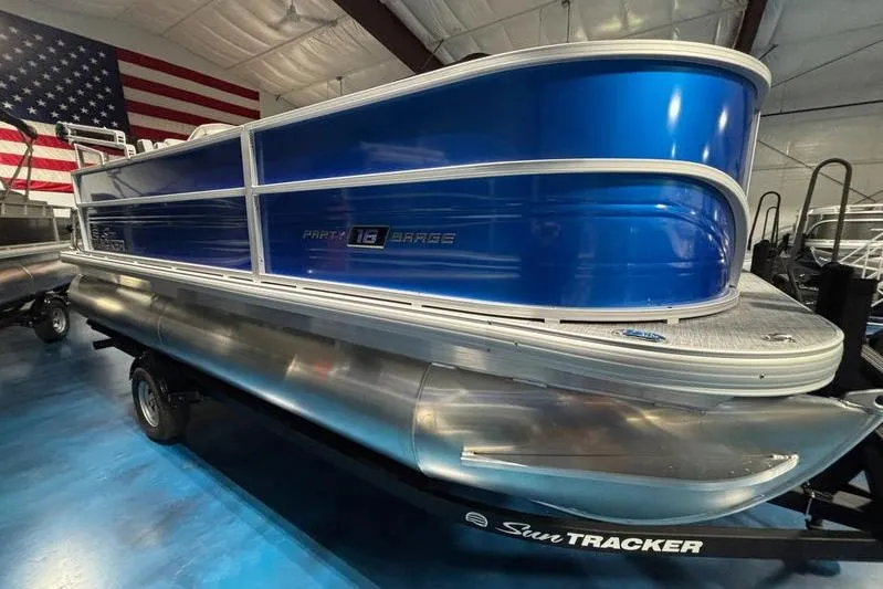 The Image of 2026 Sun Tracker Party Barge 18 DLX pontoon boat in showroom with American flag backdrop. - 0