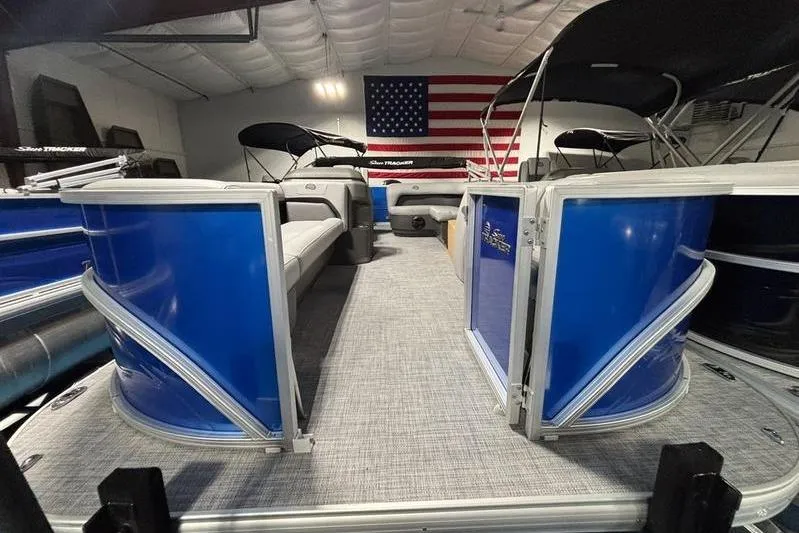 Slide: The Image of 2026 Sun Tracker Party Barge 18 DLX pontoon boat with blue exterior, indoors, American flag backdrop. - 7