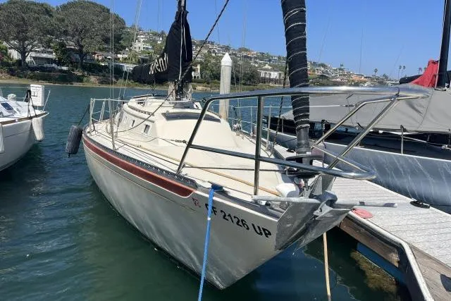 Slide: The Image of 1977 Islander 36 sailboat docked in a marina, surrounded by calm water and scenic background. - 16
