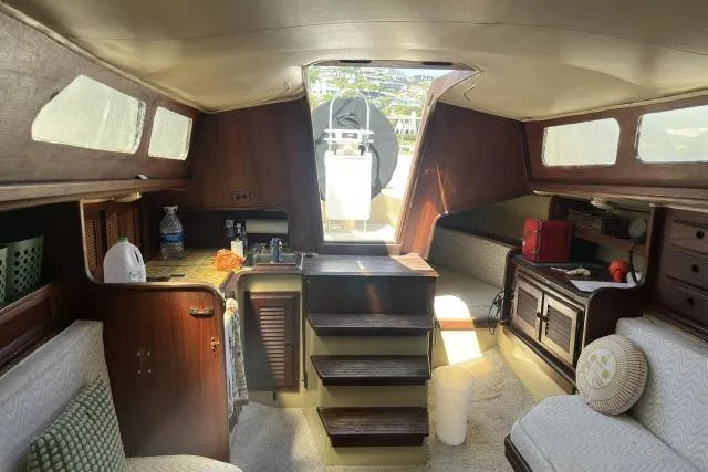 Slide: The Image of Interior of a 1977 Islander 36 sailboat, featuring cozy seating and wooden cabinetry. - 3