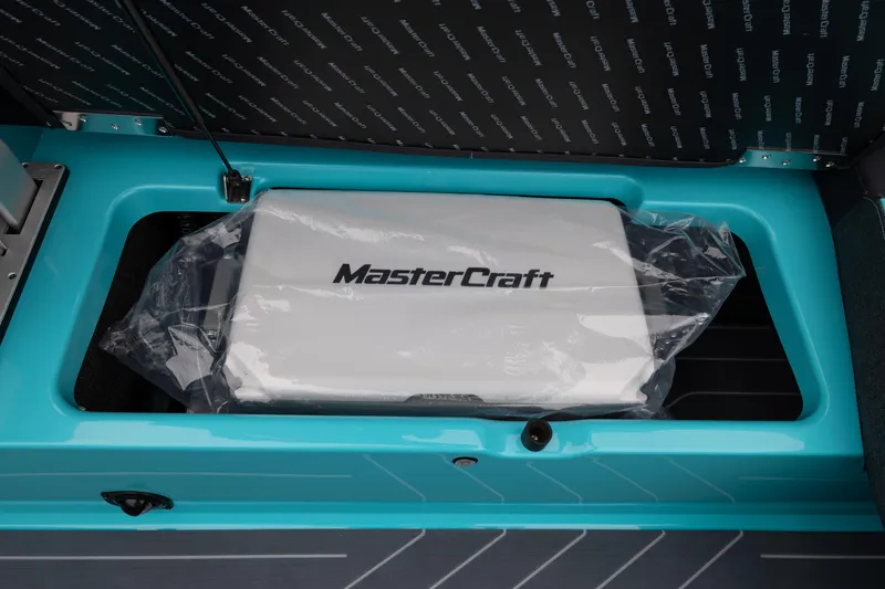 Slide: The Image of 2026 MasterCraft X24 storage compartment with branded cover in turquoise interior. - 24
