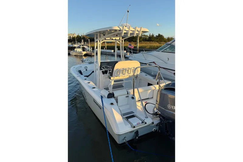 Slide: The Image of 2021 Tidewater 210 LXF boat on calm water, man steering, grassy shoreline in background. - 15