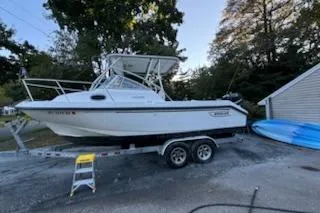 Slide: The Image of 2000 Boston Whaler 23 Conquest boat on trailer, parked outdoors near trees and a building. - 3