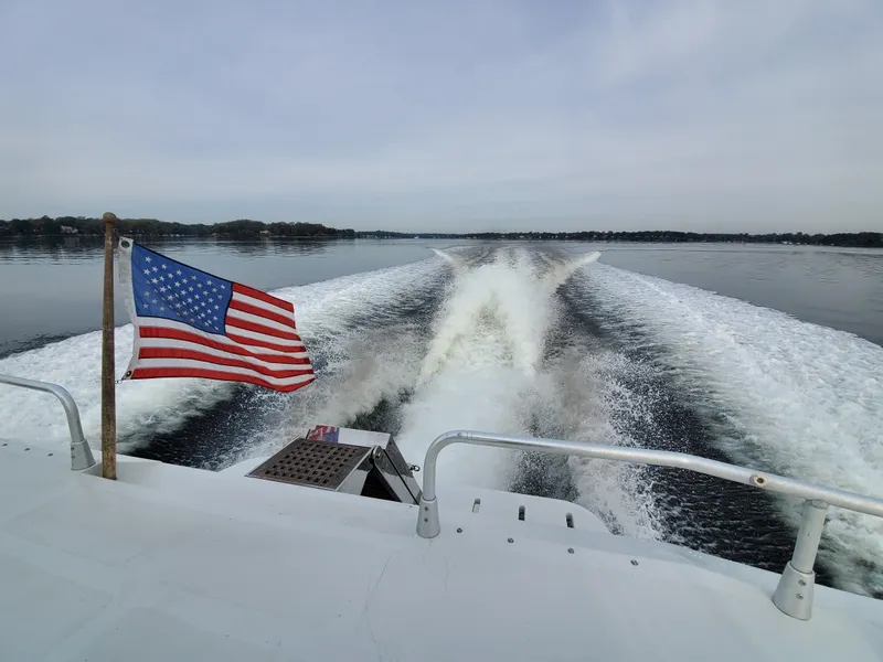 Slide: The Image of A 1993 Giorgi 46 boat cruising with an American flag, leaving a wake on a calm lake. - 7