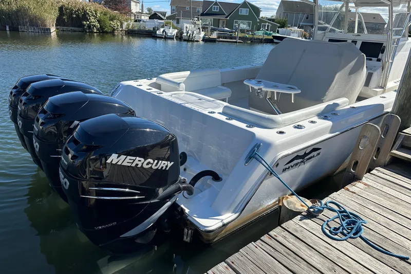 Slide: The Image of 2018 Invincible 42 boat with four Mercury outboard engines docked by the water. - 2