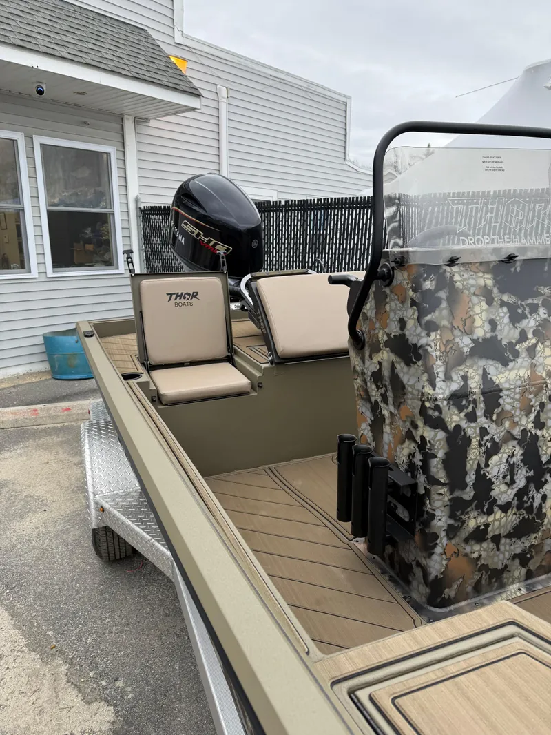 Slide: The Image of Thor 1900 boat, 2025 model, with camouflage console and beige seating, docked near a building. - 2