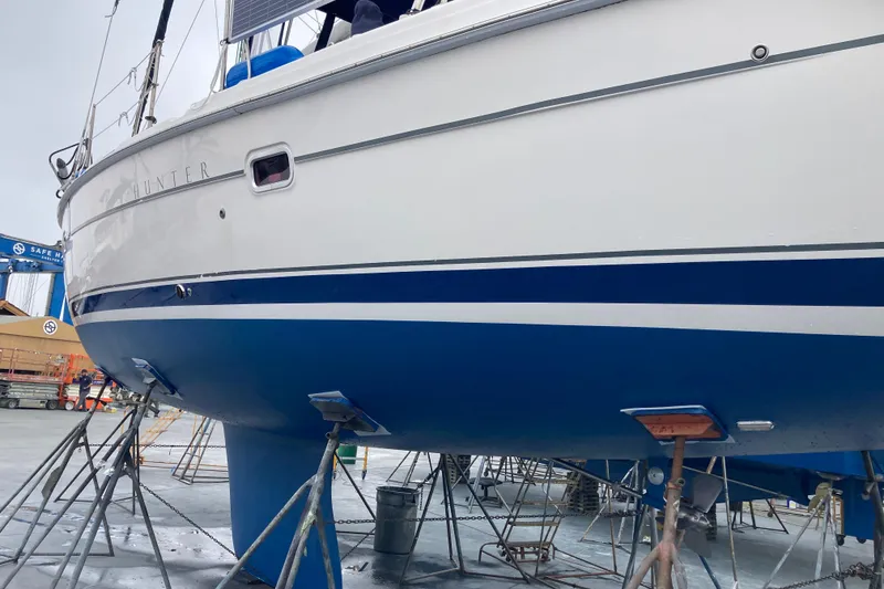 Slide: The Image of 2006 Hunter 45 CC sailboat on stands, blue and white hull, in a shipyard. - 51