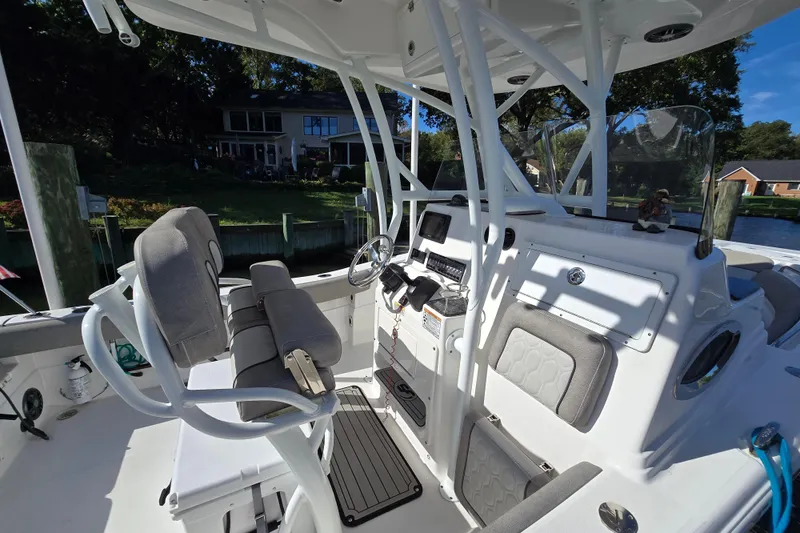 Slide: The Image of 2022 Sea Fox 249 Avenger boat interior with helm and seating, docked near waterfront homes. - 2