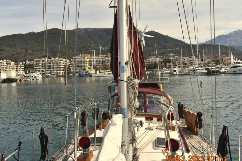 Slide: The Image of 1988 Tayana Vancouver 42 sailboat docked in a scenic marina with mountains in the background. - 2