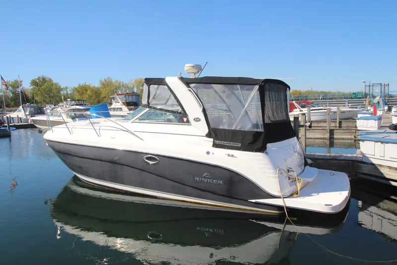 The Image of 2006 Rinker 320 Express Cruiser docked at marina, featuring sleek design and black canopy. - 0