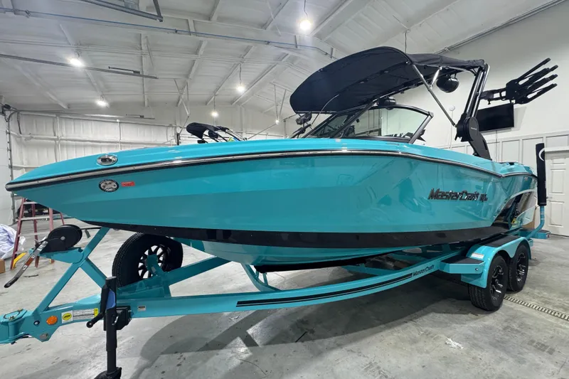 The Image of 2026 MasterCraft NXT22 boat in a showroom, vibrant turquoise color, on a matching trailer. - 1