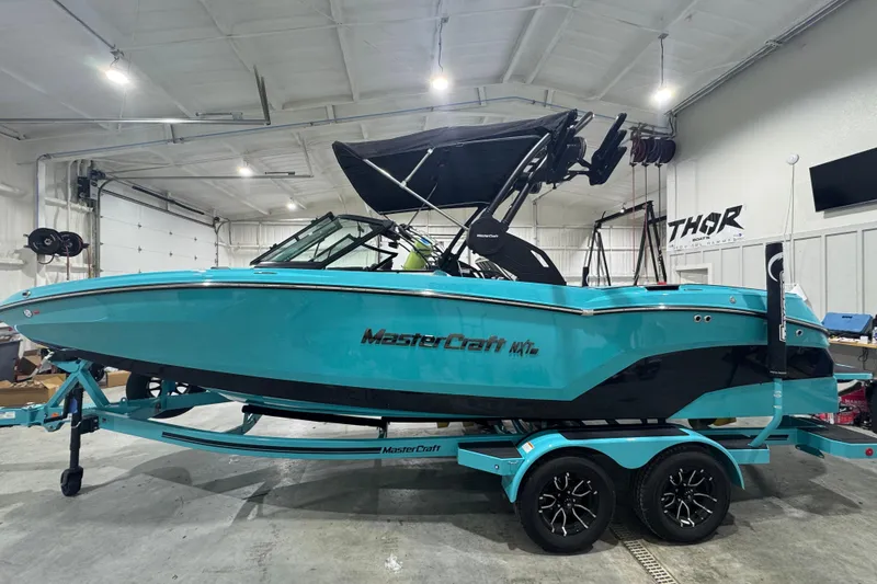 Slide: The Image of 2026 MasterCraft NXT22 boat in a garage, vibrant turquoise color, on a matching trailer. - 6