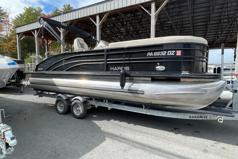 The Image of 2021 Harris Sunliner 230 pontoon boat on trailer under a covered dock. - 0