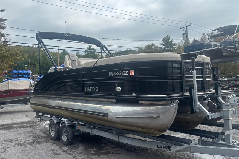 Slide: The Image of 2021 Harris Sunliner 230 pontoon boat on trailer, parked outdoors under cloudy sky. - 2