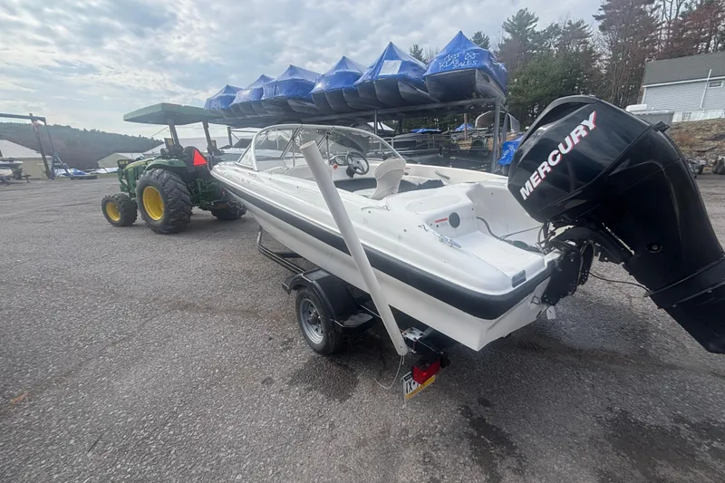 Slide: The Image of 2011 Bayliner 160 Bowrider on trailer, with Mercury outboard motor, parked near tractor. - 12