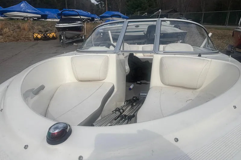 Slide: The Image of 2011 Bayliner 160 Bowrider boat interior with white seating and windshield, parked outdoors. - 16
