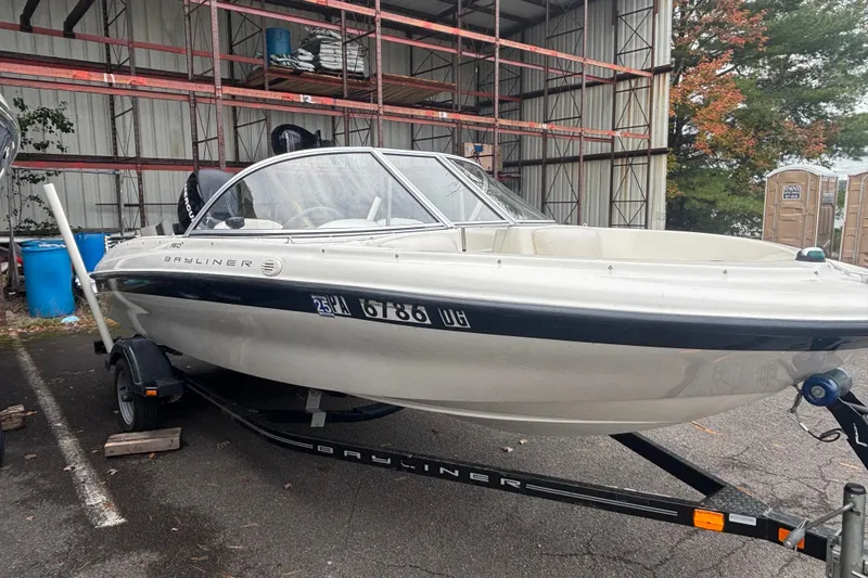 Slide: The Image of 2011 Bayliner 160 Bowrider on trailer, parked outdoors near storage racks. - 3