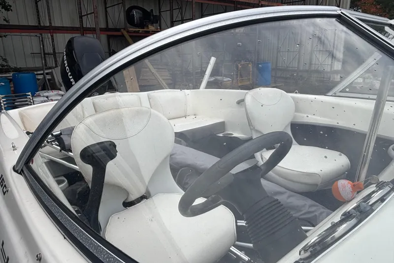 Slide: The Image of 2011 Bayliner 160 Bowrider interior with white seats and steering wheel in a storage area. - 6