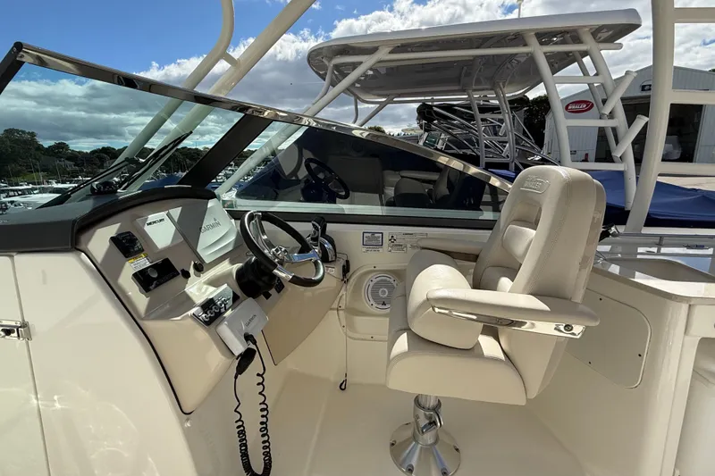 Slide: The Image of 2015 Boston Whaler 270 Vantage helm with steering wheel and captain's chair under a cloudy sky. - 13