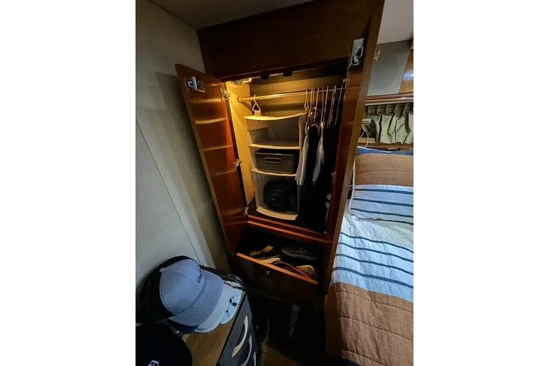 Slide: The Image of Wooden closet interior on 2003 Cruisers Yachts 4370 Express, featuring organized storage and clothing. - 19