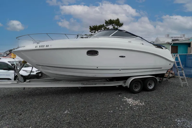 The Image of 2009 Sea Ray 250 Sundancer boat on trailer, parked on gravel, under a partly cloudy sky. - 0