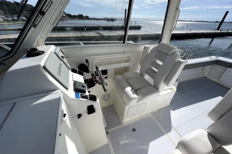 Slide: The Image of 2024 NorthCoast 235 boat interior with helm, white seating, and waterfront view. - 15