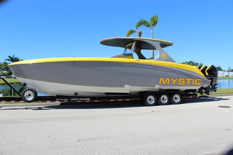Slide: The Image of 2021 Mystic M4200 boat on trailer, yellow and gray design, parked near water. - 2