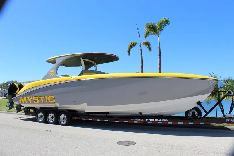 Slide: The Image of 2021 Mystic M4200 boat on trailer, yellow and gray design, palm trees in background. - 9