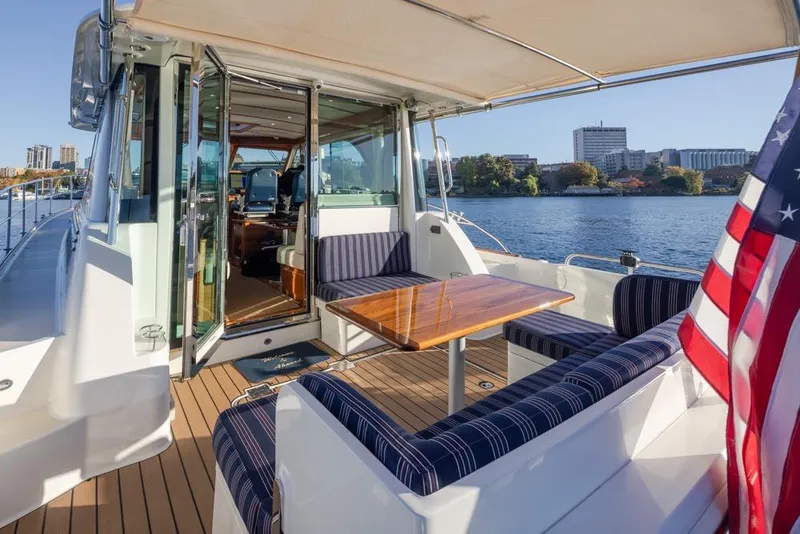 Slide: The Image of 2020 Sabre 45 Salon Express yacht with outdoor seating, wooden table, and American flag by the water. - 13
