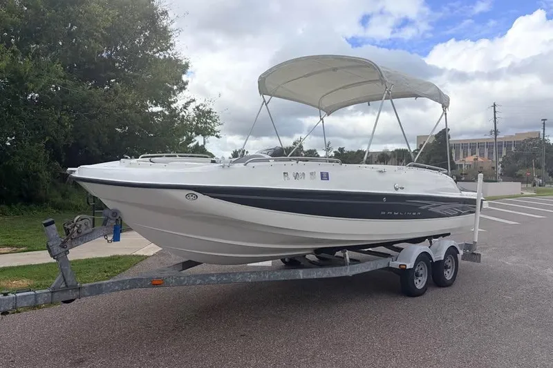 The Image of 2007 Bayliner 217 Deck Boat on trailer, parked outdoors under cloudy sky. - 0
