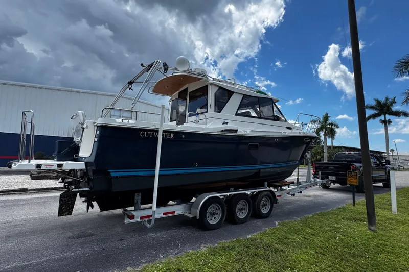 Slide: The Image of 2019 Cutwater C-28 boat on trailer under cloudy sky, parked near palm trees. - 2