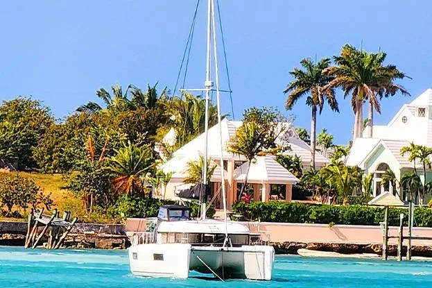 Slide: The Image of 2018 Lagoon 40 catamaran sailing near tropical waterfront homes and palm trees. - 2
