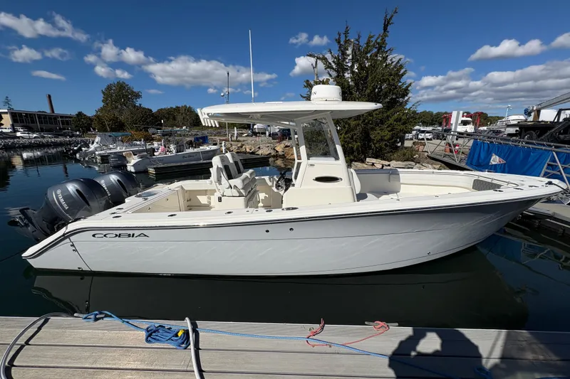 Slide: The Image of 2022 Cobia 280 Center Console boat docked, featuring twin Yamaha engines under a clear blue sky. - 48