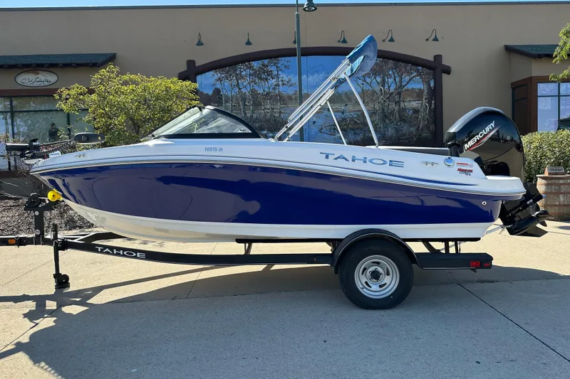 Slide: The Image of 2024 Tahoe 185 S boat on trailer, blue and white design, parked outdoors. - 0