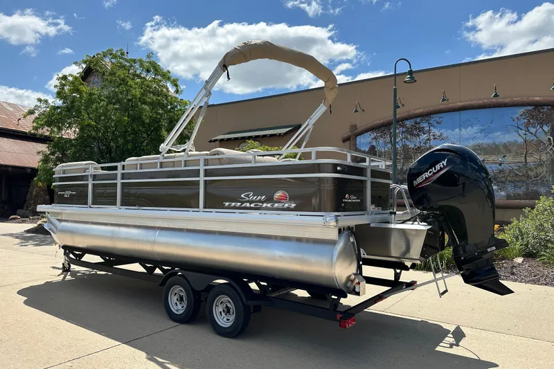 Slide: The Image of 2025 Sun Tracker SportFish 22 DLX pontoon boat on trailer, outdoors, sunny day. - 2